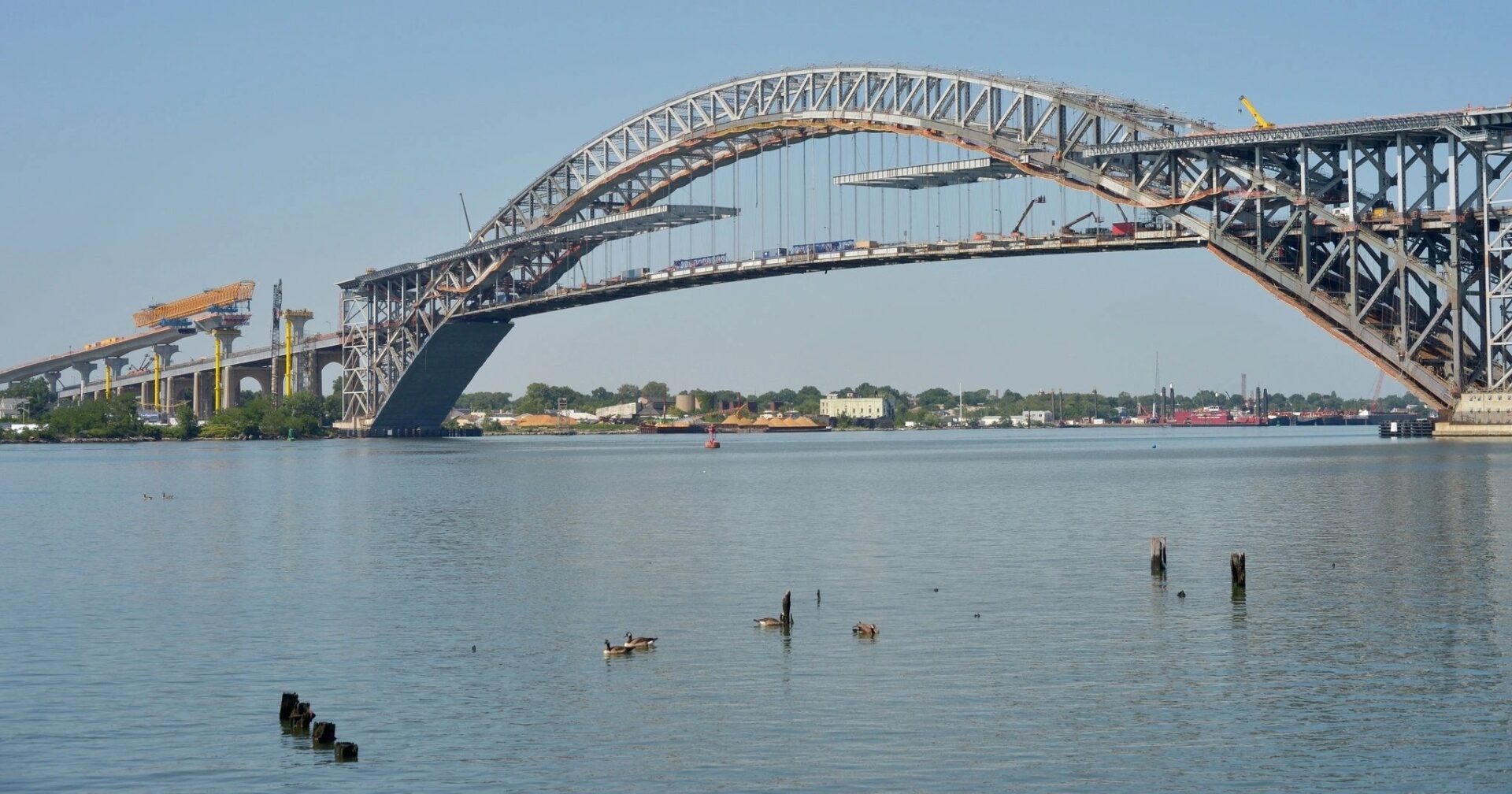 A person on a surfboard in the water under a bridge.